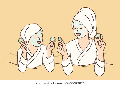 Two girls with hygienic mask on face rest lying on bed during rejuvenating spa treatment. Young mom and daughter in bathrobes use cosmetic masks to prevent wrinkles and get rid of acne