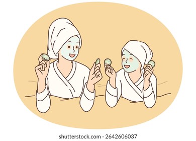 Two girls with hygienic mask on face rest lying on bed during rejuvenating spa treatment. Young mom and daughter in bathrobes use cosmetic masks to prevent wrinkles and get rid of acne