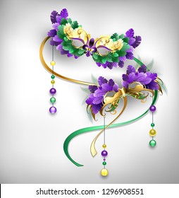 Two gold, carnival masks, decorated with purple and green feathers on gray background. Fat Tuesday. Mardi Gras.