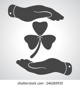two hands with  Clover with three leaves sign icon. on a grey background. Saint Patrick symbol