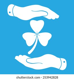 two hands with Clover with three leaves sign icon. on a blue background. Saint Patrick symbol