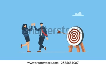 Two happy employees claping hands, hi five  each other next to a target board simbolyzes team success winners, hi five or congratulation on business goal achievement, collaboration or encouragement.