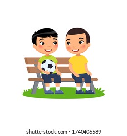 Two little Asian boys with soccer ball sit on bench. Summer holidays, recreation, sports, hobbies. 