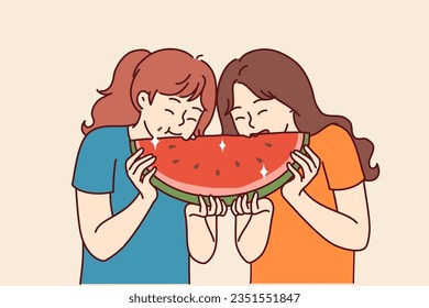 Two little girls are eating watermelon and laughing, enjoying large piece of sweet refreshing fruit. Kids are friends and together enjoy cold snack with watermelon in hot summer weather