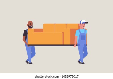 two mix race couriers in uniform moving couch express delivery service concept professional furniture movers holding new sofa flat full length horizontal