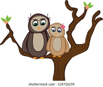 Two owls are in a tree with some fresh spring leaves and a few flowers. One owl has a flower in her feathers.