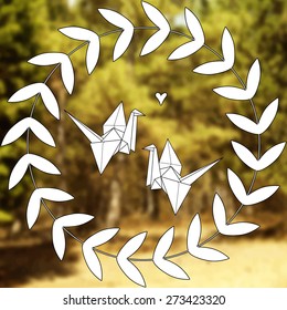 Two paper origami cranes on the blurred forest background in the floral frame.