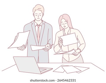 Two skilled professionals are diligently collaborating on important documents at a desk equipped with a laptop