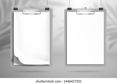 Two white blank notebooks is clamped in the clipboards and hanging on the clips above the surface. The shadow of the palm tree leaf falls on the wall behind. Mockup for design
