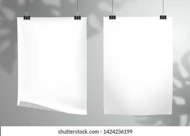 Two white blank realistic sheet of paper hang on clips. The shadow of the Monstera plant falls on the wall behind. Mockup for design