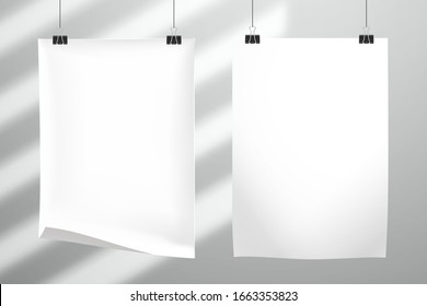 Two white blank realistic sheet of paper hang on clips. The shadow from the blinds falls on the wall behind. Mockup for design