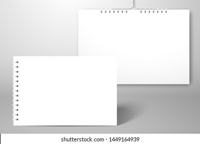 Two white blank spiral notebooks, albums or calendars. One stands on the surface, the second hangs near the wall.  Mockup for design with shadow
