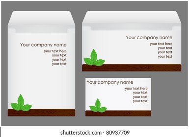 Two white envelope, business card with a wooden plaque and green leaves