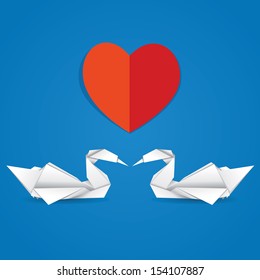  Two white paper swans and red heart on blue background.