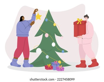 Two woman preparing for the new year, one of them decorating a Christmas tree for the holiday, hanging Christmas toys and the second puts gifts under the Christmas tree ,
