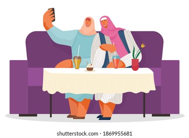 Two women friends wearing hijabs taking selfie together at phone. Arab women sitting at sofa in cafe or restaurant, drinking lemonade, eating cupcake. People spend leisure time. Isolated characters