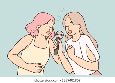 Two women sing song in karaoke at house party. I get positive emotions from musical leisure. Young cheerful girls with microphone enjoy singing in karaoke club or professional recording studio 