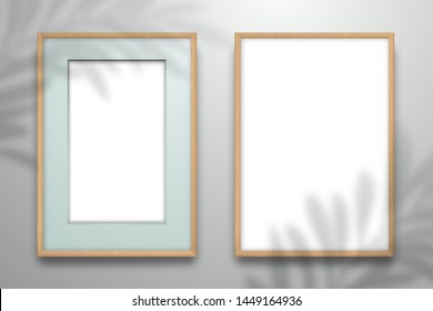 Two wooden frames with colored passe-partout and without it for an image or photo hanging on the wall. The shadow of the palm tree leaf is on top. Mockup for design