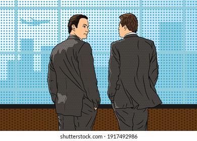 Two young business men in suits stand in the office near the window, look at the city and has a conversation.