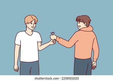 Two young guys bump their fists when they meet, making greeting to members of student fraternity. Positive teenage boys in casual clothes say goodbye after fun together walk