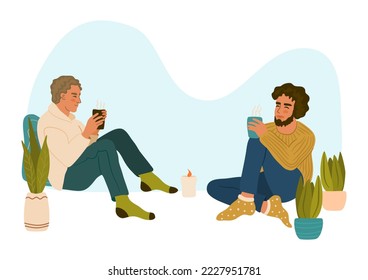 Two young men sitting, talking and drinking hot drink. Cozy date on a cold evening. Hygge lifestyle concept.