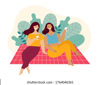 Two young women are sitting on a plaid in a park. Friends are laughing and talking. Concept of a picnic, relaxing at the weekend. Basket with food, hat and ball. Flat color vector illustration.