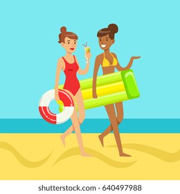Two young women walking on the beach holding lifebuoy and floating mattress