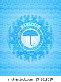 umbrella icon inside sky blue water wave emblem background.