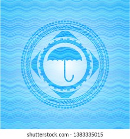 umbrella icon inside sky blue water wave emblem background.