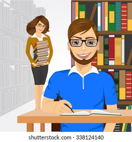 university male student with open book styding in the college library and young happy librarian with glasses holding stack of books cstanding behind him