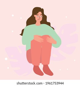 Upset, saddened, the girl sits with her hands clasped around her knees.
