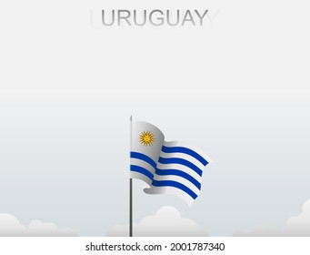 The Uruguayan flag flutters on a pole that stands tall under a white sky