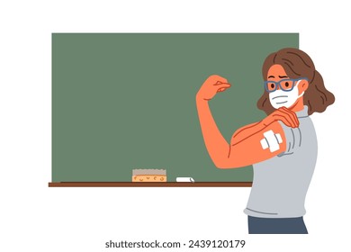 Vaccinated female teacher demonstrates patch at injection site on arm, standing near school board. Vaccinated girl teacher recommends taking preventive measures to protect against virus
