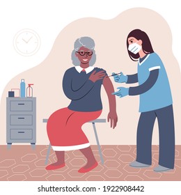 Vaccination procedure. Caucasian female nurse administering a vaccination shot to a patient. Young woman doctor in a face mask holding a syringe and an elderly black woman with outstretched arm.