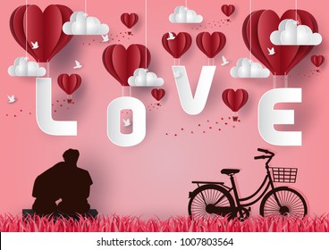 Valentine's Day Concept Boy and girl sitting on a table with a bike. Look up at the sky and point to the balloon floating in the pink sky with the letters L O V E and flying birds have hearts. paper