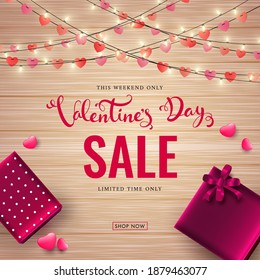 Valentine's Day Sale Text with Top View of Gift Boxes, Hearts and Lighting Garlands Decorated on Glossy Brown Wooden Texture Background.