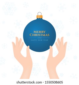 Vector blue Christmas bulb in hands with text Merry Christmas And Happy New Year. White isolated background with snowflakes.  