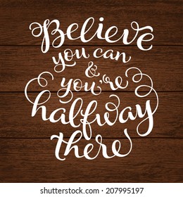 Vector calligraphic inscription with ornamental elements on wood background. "Believe you can and you're halfway there" poster or postcard. Typography collection