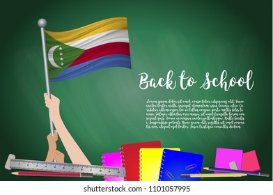Vector flag of Comoros on Black chalkboard background. Education Background with Hands Holding Up of Comoros flag. Back to school with pencils, books, school items learning and childhood concept.