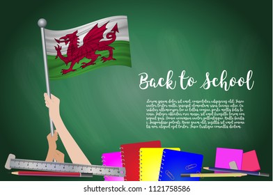 Vector flag of Wales on Black chalkboard background. Education Background with Hands Holding Up of Wales flag. Back to school with pencils, books, school items learning and childhood concept.