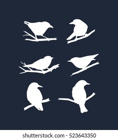 Vector graphic set of hand drawn birds sitting on branches. White silhouettes on dark background. Papercut style.