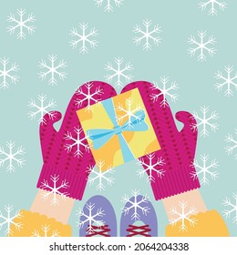 Gráficos vectores - una hermosa tarjeta de vacaciones - caja de regalo con un arco en las manos de mitones de punto y copos de nieve cayendo del cielo. Concepto: Navidad y Año Nuevo