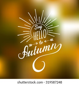 Vector hand lettering inspirational typography poster Say hello to autumn with rays on blurred background.