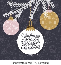 Vector holiday background with hanging Christmas ornaments, fir branch and handwritten text ‘Wishing you a Merry Christmas’. Winter greeting card with decorations and wishes.