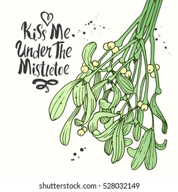 Vector holiday illustration Kiss Me Under the mistletoe on white background with green branch. Handwritten inscription. Lettering design. Sketch style.