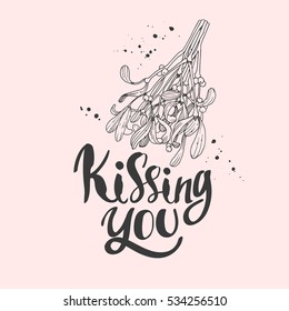 Vector holiday illustration Kissing You on pink background with green branch of mistletoe. Handwritten inscription. Lettering design. Sketch style.