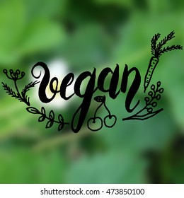 Vector lettering vegan made with brush pen with flowers, leaves, carrot on green blurred background. Inscription vegan.