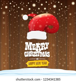 vector red Santa hat with greeting text Merry Christmas and happy new year on wooden background with falling snowflakes. Funny Merry christmas greeting card, banner or poster xmas background.