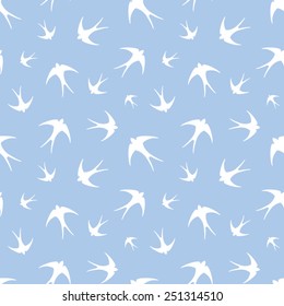 Vector seamless pattern with white silhouettes of swallows on a blue background.