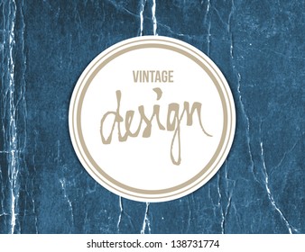Vector vintage crumpled paper sticker with handwritten word "design" over old distressed blue cardboard background